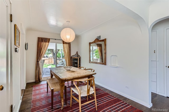 dining room featuring dark wood-type flooring, arched walkways, and baseboards