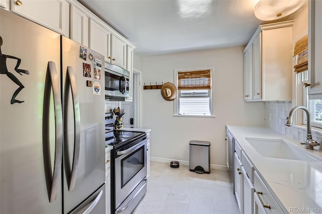 kitchen with appliances with stainless steel finishes, a sink, baseboards, and healthy amount of natural light
