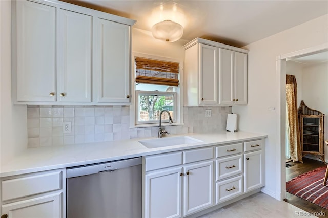 kitchen featuring stainless steel dishwasher, a sink, decorative backsplash, light countertops, and white cabinets