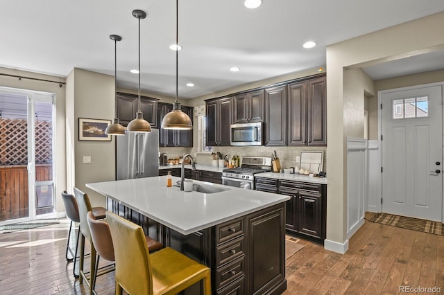 kitchen with appliances with stainless steel finishes, sink, a breakfast bar area, hanging light fixtures, and a kitchen island with sink