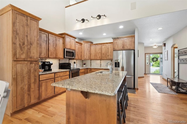 641 Denali Ct, Windsor, CO 80550 - kitchen featuring stainless steel appliances, a sink, light wood-style floors, a breakfast bar area, and light stone countertops