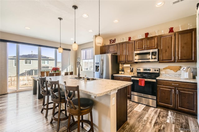 kitchen featuring appliances with stainless steel finishes, sink, decorative light fixtures, and an island with sink