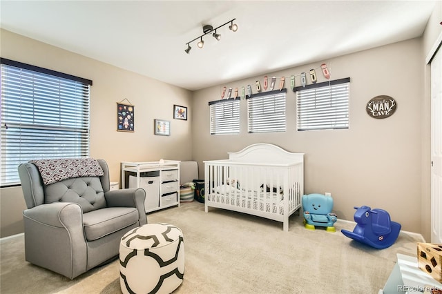 carpeted bedroom featuring rail lighting and a crib