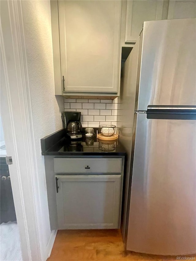 kitchen with stainless steel fridge, backsplash, white cabinetry, and light hardwood / wood-style flooring