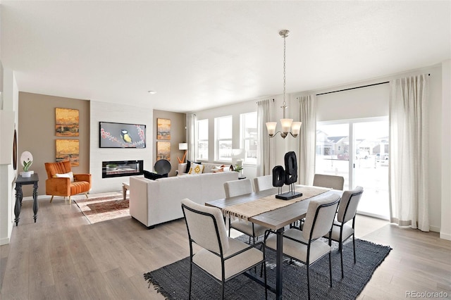 dining space with light wood-style flooring, a large fireplace, a chandelier, and baseboards