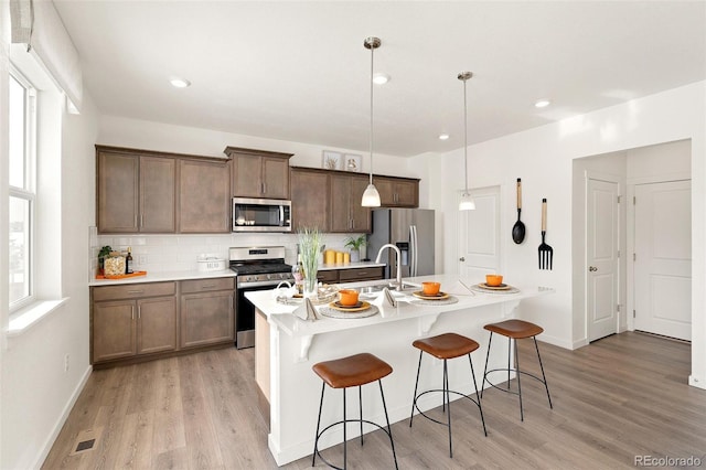 kitchen featuring appliances with stainless steel finishes, light wood-style flooring, decorative backsplash, a kitchen breakfast bar, and recessed lighting