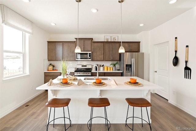kitchen with appliances with stainless steel finishes, a sink, a breakfast bar area, light countertops, and recessed lighting