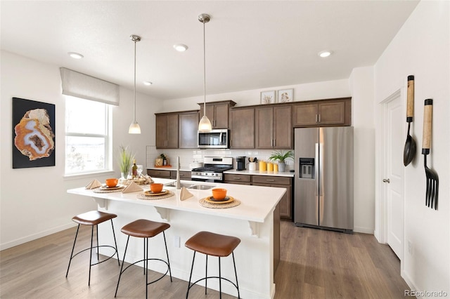 kitchen featuring stainless steel appliances, a kitchen breakfast bar, light countertops, tasteful backsplash, and light wood finished floors