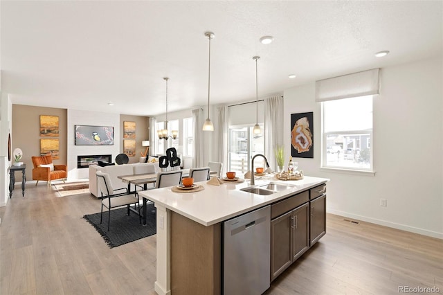 kitchen featuring a sink, dishwasher, a kitchen island with sink, light wood finished floors, and light countertops