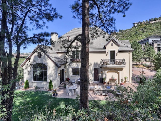 back of house with a balcony, a patio area, and a lawn