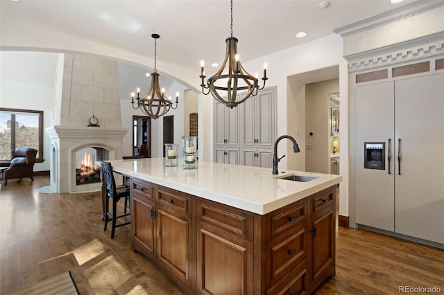 kitchen featuring a fireplace, sink, dark hardwood / wood-style flooring, paneled refrigerator, and a center island with sink