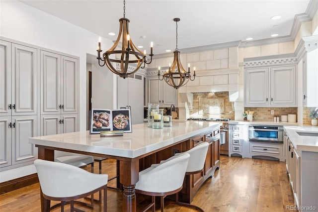 kitchen featuring decorative light fixtures, tasteful backsplash, a kitchen bar, light wood-type flooring, and a spacious island