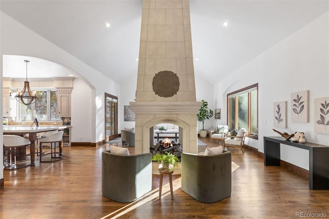 living room featuring dark wood-type flooring, a multi sided fireplace, an inviting chandelier, and high vaulted ceiling