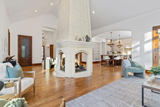 living room with hardwood / wood-style flooring, a multi sided fireplace, high vaulted ceiling, and an inviting chandelier