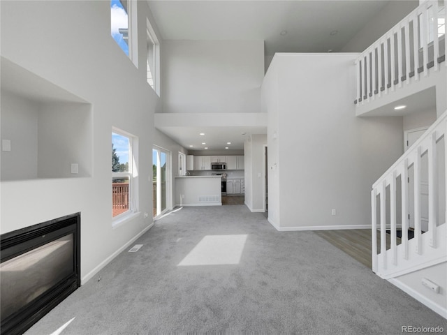 unfurnished living room featuring a high ceiling and light colored carpet