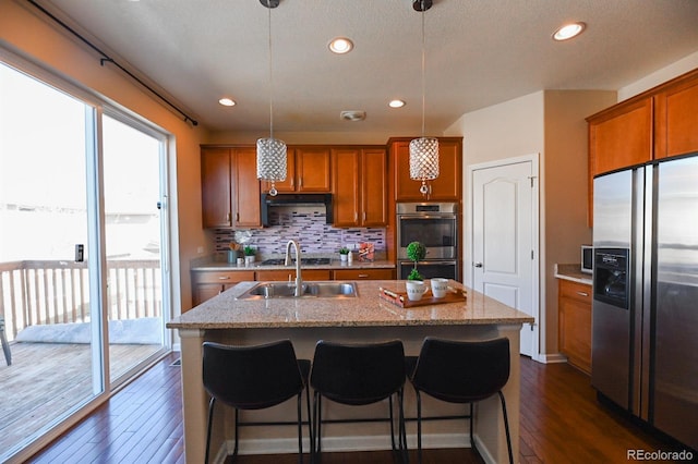 kitchen featuring an island with sink, appliances with stainless steel finishes, brown cabinets, and a sink