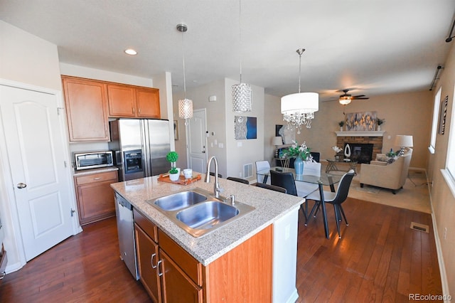 kitchen featuring a stone fireplace, stainless steel appliances, a sink, open floor plan, and brown cabinets