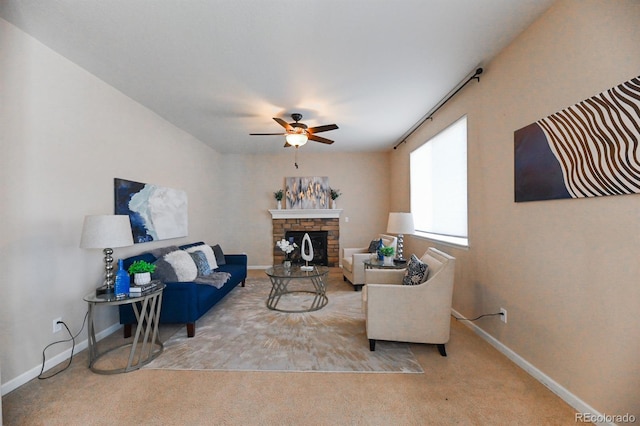 living room with carpet, baseboards, ceiling fan, and a stone fireplace