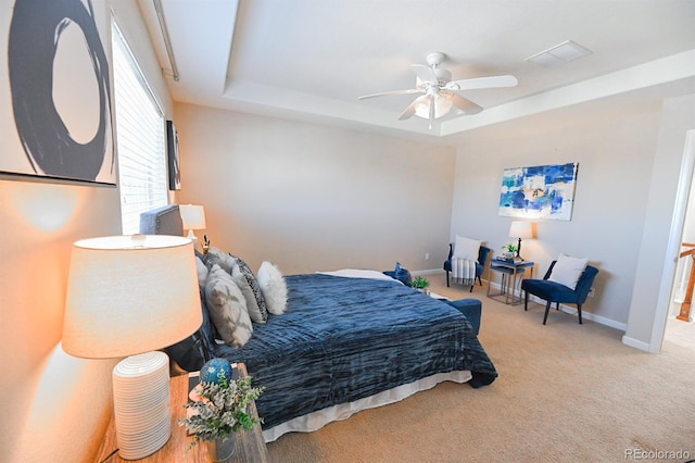 carpeted bedroom featuring a ceiling fan, visible vents, a tray ceiling, and baseboards