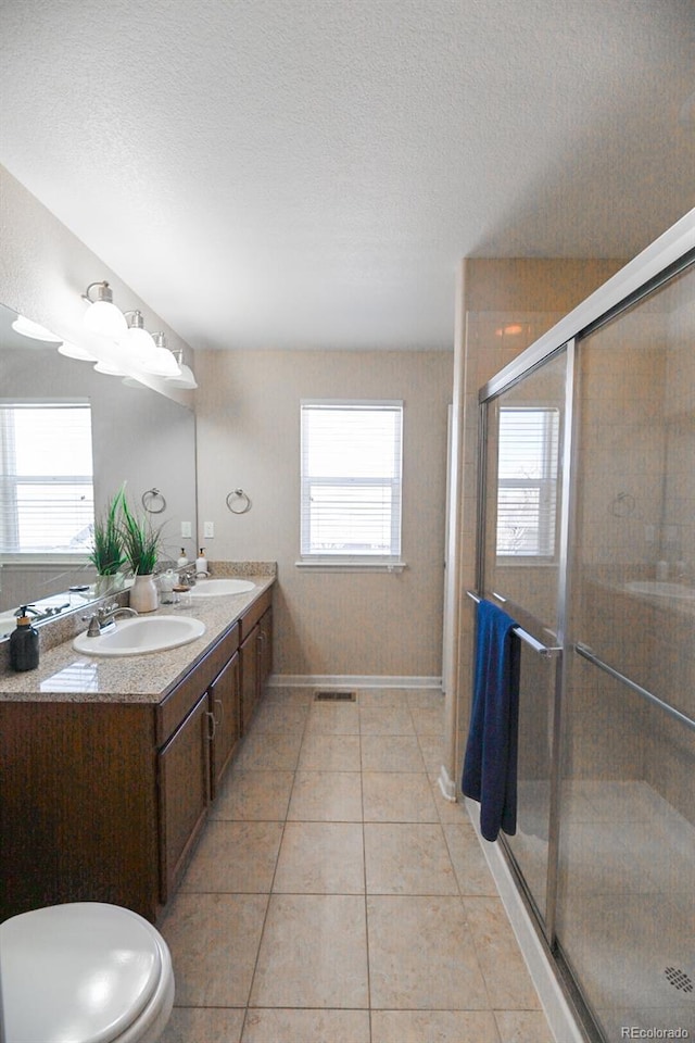 full bathroom with a stall shower, a textured ceiling, a sink, and tile patterned floors