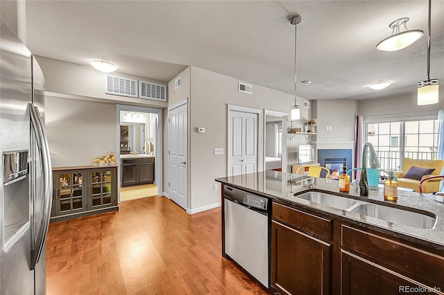 kitchen with dark brown cabinetry, appliances with stainless steel finishes, a sink, wood finished floors, and a tile fireplace