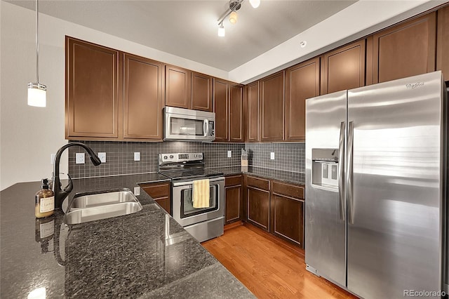 kitchen featuring appliances with stainless steel finishes, a sink, light wood-style flooring, and tasteful backsplash