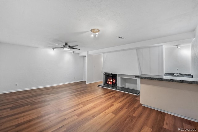 unfurnished living room with a lit fireplace, wood finished floors, a ceiling fan, baseboards, and wet bar