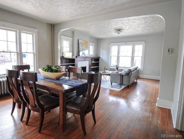 dining area featuring arched walkways, a textured ceiling, a fireplace, baseboards, and wood finished floors