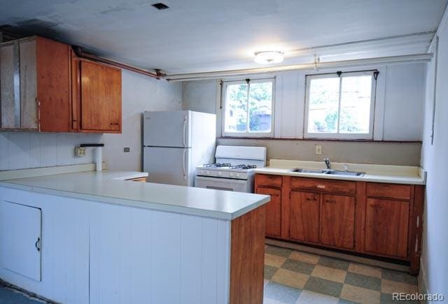 kitchen with white appliances, a sink, light flooring, light countertops, and a peninsula