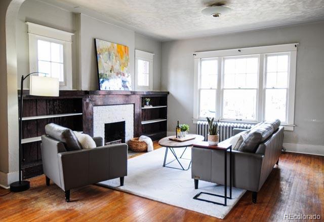 living room with wood-type flooring, a brick fireplace, a textured ceiling, radiator heating unit, and baseboards
