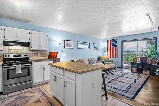 kitchen with open floor plan, under cabinet range hood, white cabinetry, and stainless steel range with electric cooktop