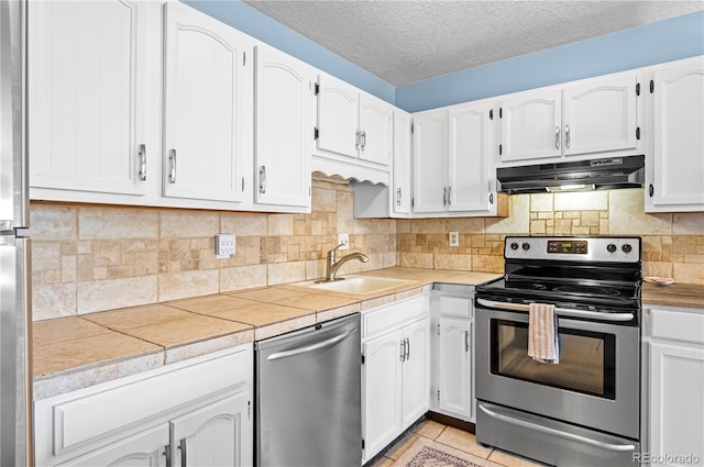 kitchen with stainless steel appliances, white cabinets, under cabinet range hood, and decorative backsplash