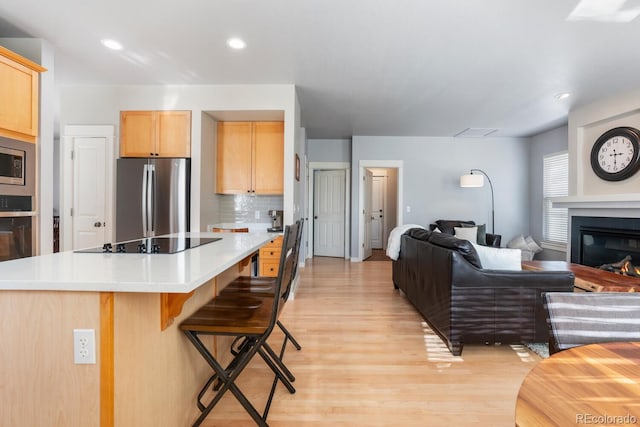 kitchen featuring a breakfast bar, stainless steel appliances, light brown cabinetry, and light hardwood / wood-style flooring