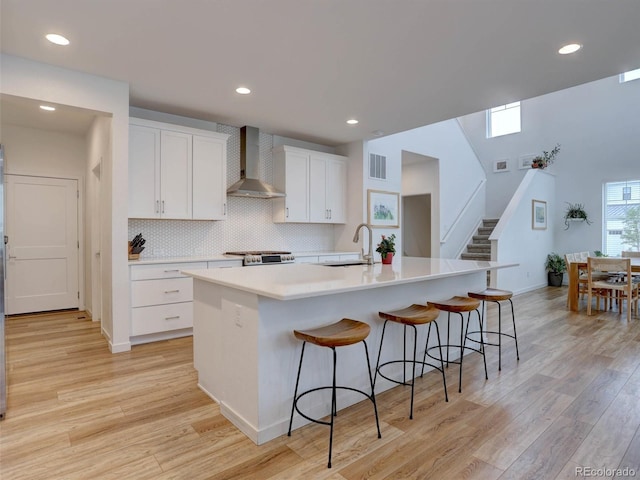 11246 Bellsong Ln, Littleton, CO 80125 - kitchen with wall chimney range hood, white cabinets, light wood finished floors, a center island with sink, and a kitchen breakfast bar