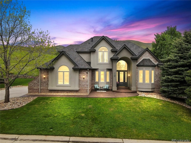 10 Summit Ash, Littleton, CO 80127 - view of front of house featuring a shingled roof, a yard, stucco siding, brick siding, and a patio