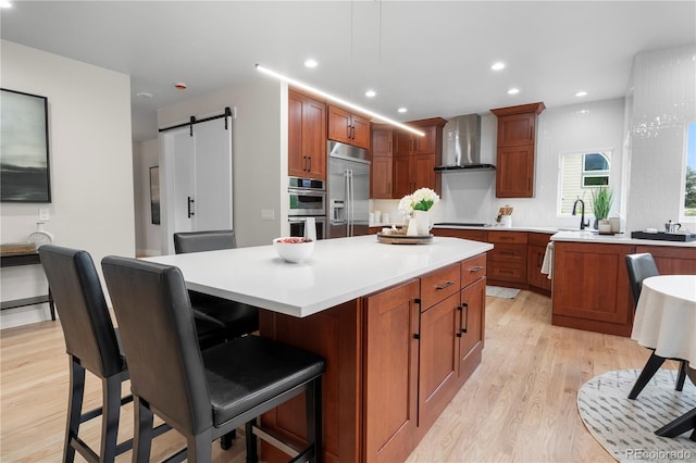 10 Summit Ash, Littleton, CO 80127 - kitchen with stainless steel appliances, wall chimney range hood, light wood-style floors, a kitchen island, and a sink