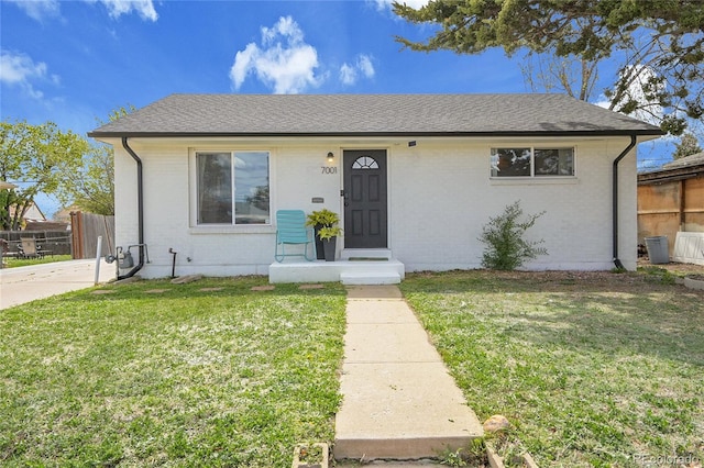 bungalow with brick siding, fence, a front yard, and roof with shingles