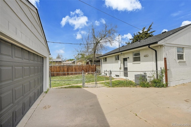 view of side of property with fence, brick siding, a garage, a gate, and central AC unit