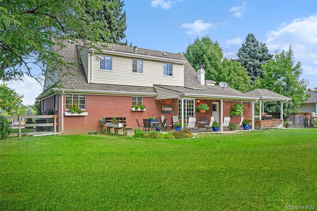 back of property featuring brick siding, a shingled roof, fence, a yard, and a patio