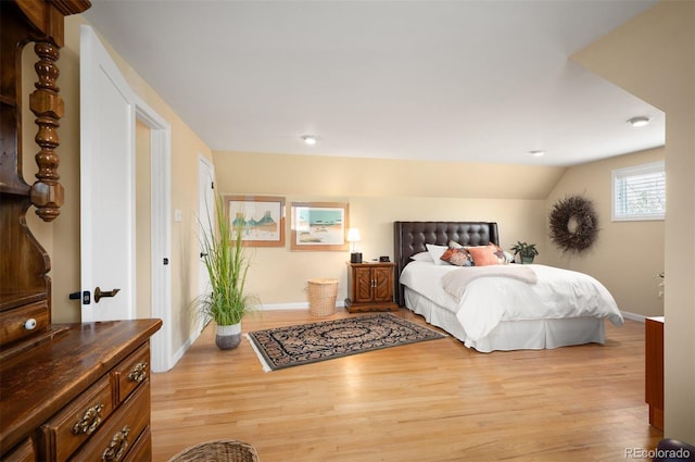 bedroom with light wood-type flooring, baseboards, and vaulted ceiling