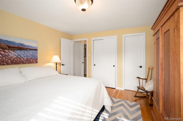 bedroom featuring baseboards, two closets, and light wood-style floors