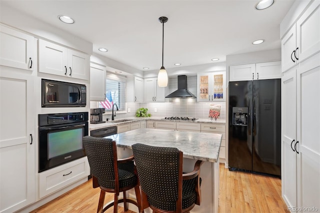 kitchen with light wood-style flooring, black appliances, wall chimney range hood, and a sink