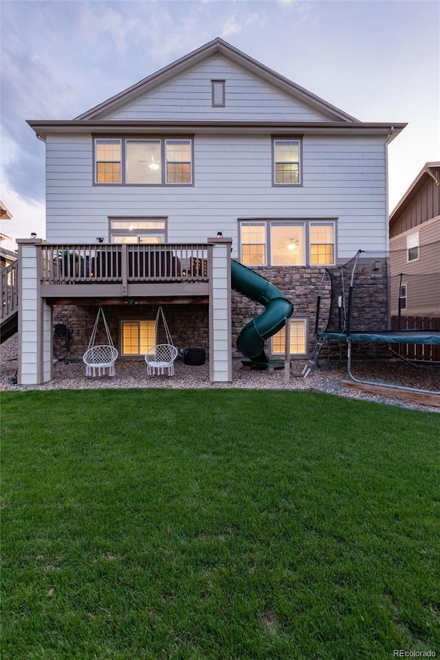 6236 S Millbrook Way, Aurora, CO 80016 - rear view of property featuring a trampoline, a deck, a lawn, and stone siding
