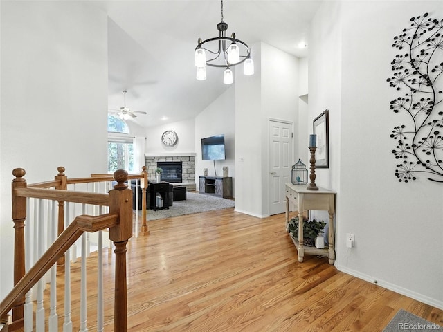 hallway featuring high vaulted ceiling, a chandelier, light wood-style floors, and an upstairs landing
