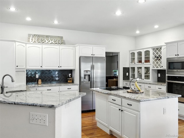 kitchen with appliances with stainless steel finishes, a center island, light wood-type flooring, white cabinets, and backsplash