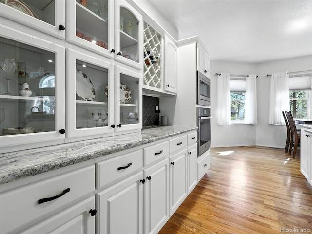 kitchen with stainless steel appliances, light wood-style flooring, white cabinetry, glass insert cabinets, and tasteful backsplash