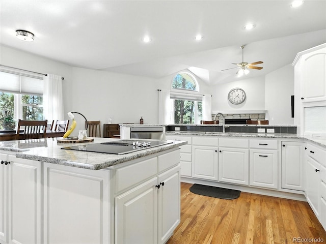 kitchen featuring black electric cooktop, lofted ceiling, a kitchen island, ceiling fan, and light wood-style flooring