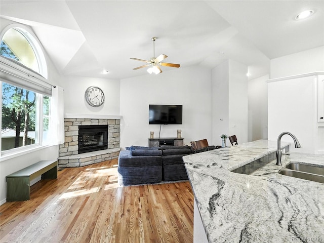 living area featuring vaulted ceiling, light wood-style floors, a ceiling fan, and a stone fireplace