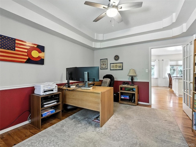 home office featuring wood finished floors, ceiling fan, and a raised ceiling