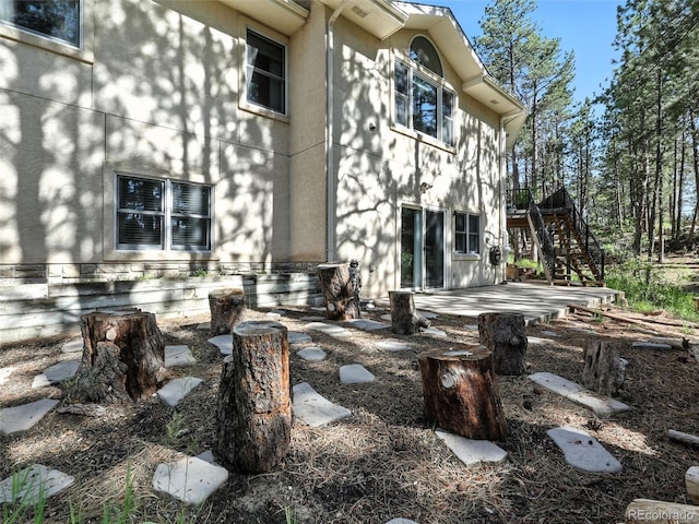 rear view of property featuring stairs, a patio, and stucco siding